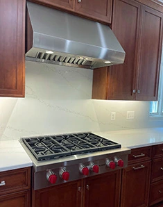 Custom kitchen remodel in Northern Virginia featuring wood cabinetry, white quartz countertops and backsplash, and stainless steel gas range with red knobs
