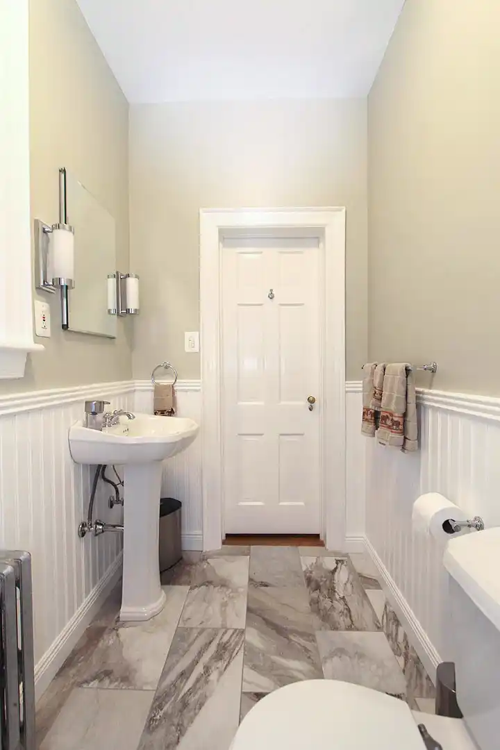 1930s Manassas VA hall bathroom remodel with pedestal sink, beadboard wainscoting, gray walls, chrome fixtures, and patterned floor tile