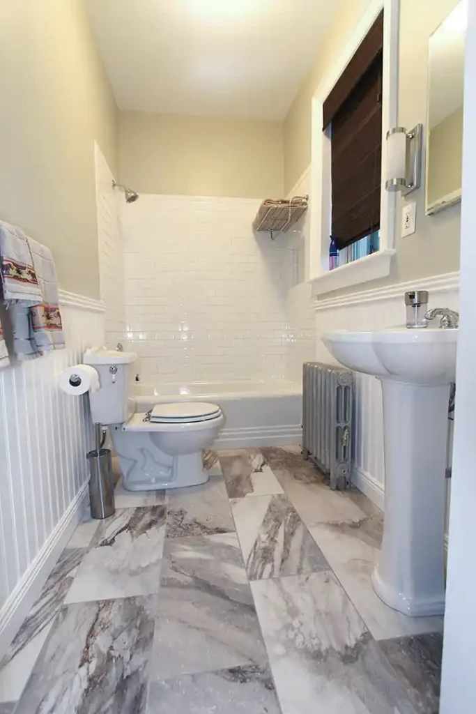 1930s Manassas VA hall bathroom remodel with pedestal sink, white subway tile tub surround, beadboard wainscoting, radiator, and patterned floor tile