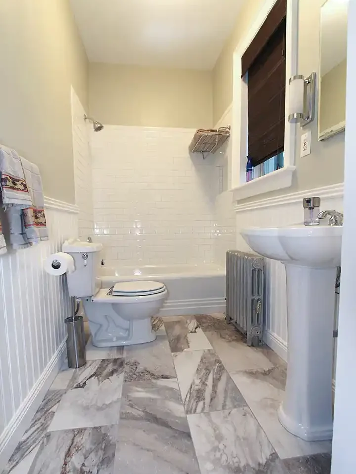 1930s Manassas VA hall bathroom remodel with pedestal sink, white subway tile tub surround, beadboard wainscoting, radiator, and patterned floor tile