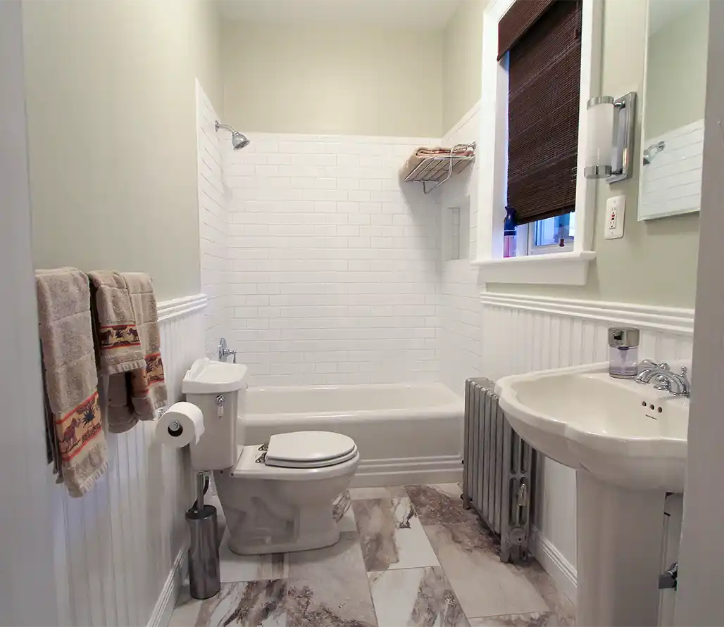 1930s Manassas VA hall bathroom remodel with white subway tile tub surround, beadboard wainscoting, pedestal sink, and vintage radiator