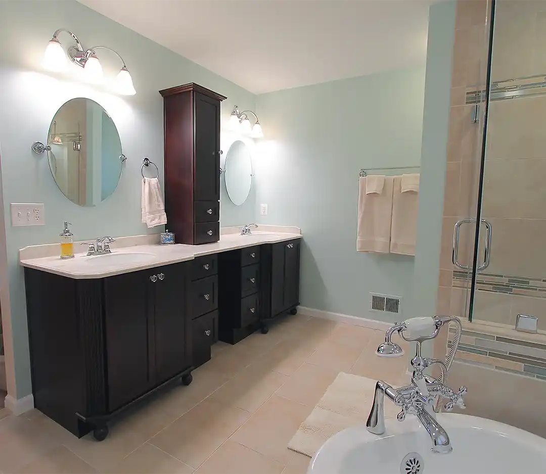 Bristow VA primary bathroom remodel with dark double vanity, tall center storage cabinet, glass tile shower, soaking tub, and chrome fixtures