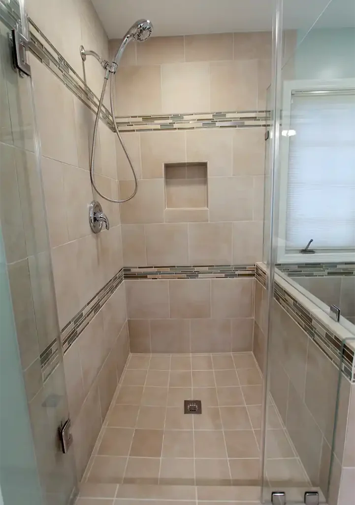 Bristow VA primary bathroom remodel with glass-enclosed tile shower, recessed niche, mosaic accent bands, and chrome shower fixtures