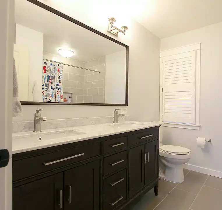 Gainesville VA bathroom remodel with dark double vanity, marble-look countertop, large framed mirror, tile tub shower, and shuttered window