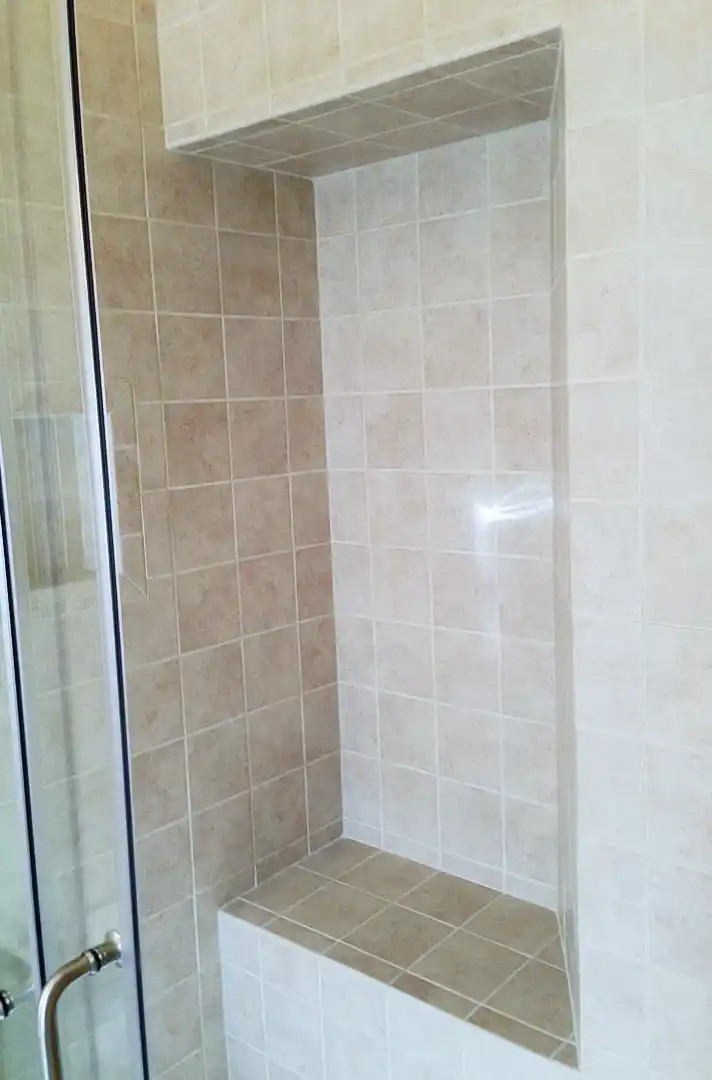 Gainesville VA bathroom remodel with tiled shower bench, neutral wall tile, glass shower door, and built-in shower seating