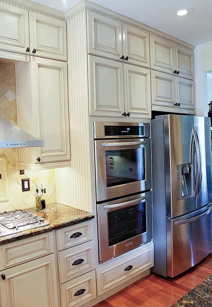 Gainesville VA kitchen remodel with cream cabinets, built-in double oven, stainless refrigerator, gas cooktop, granite countertops, and tile backsplash