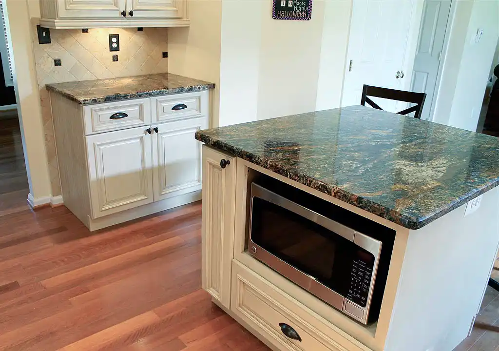 Gainesville VA kitchen remodel with granite island, built-in microwave cabinet, cream cabinetry, tile backsplash, and wood flooring