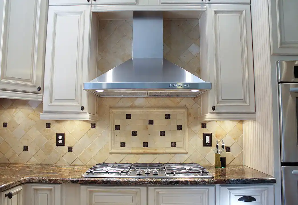 Gainesville VA kitchen remodel with stainless range hood, gas cooktop, cream cabinets, granite countertops, and decorative tile backsplash