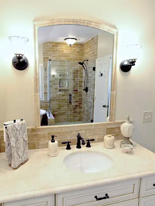 Gainesville VA primary bathroom remodel with cream vanity, arched tile mirror, dark bronze fixtures, and tile shower reflection