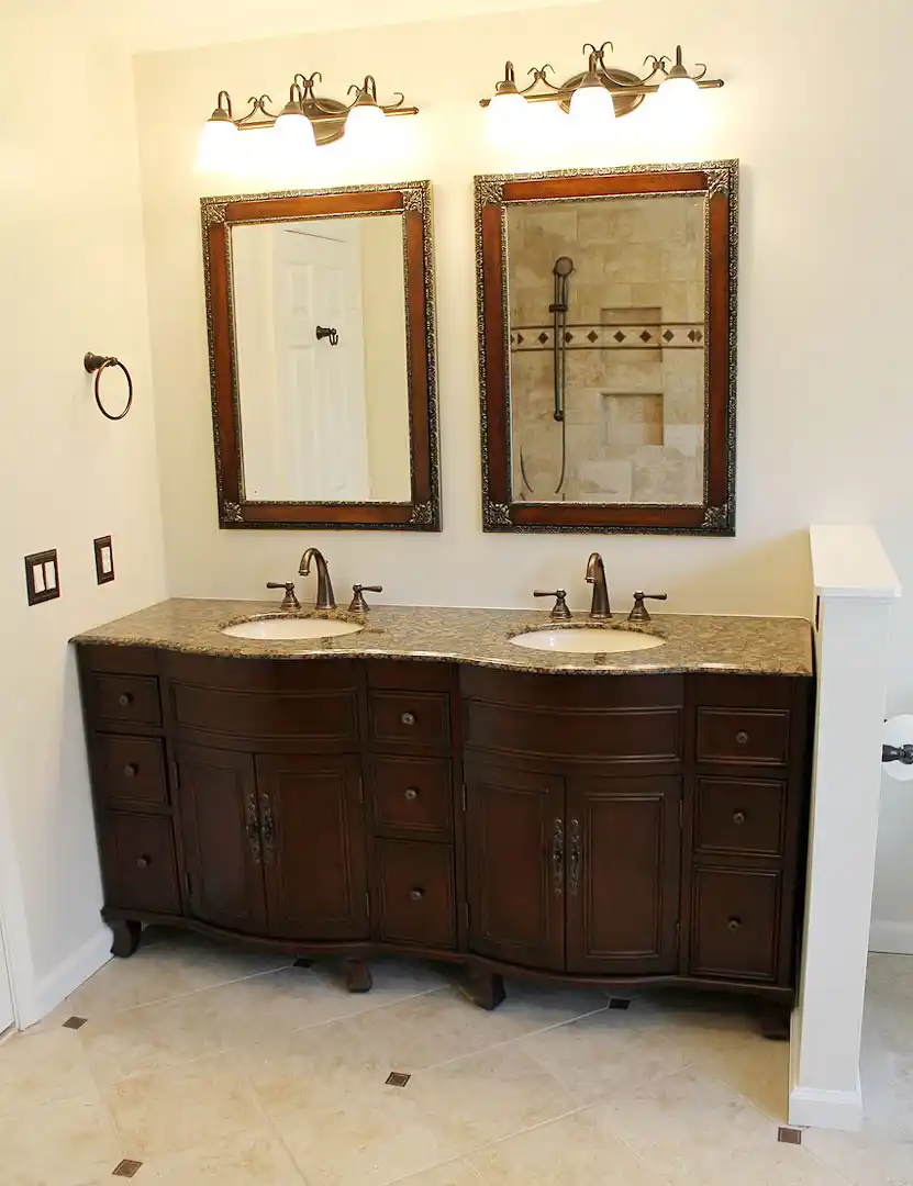 Gainesville VA primary bathroom remodel with dark wood double vanity, granite countertop, framed mirrors, bronze fixtures, and wall lights