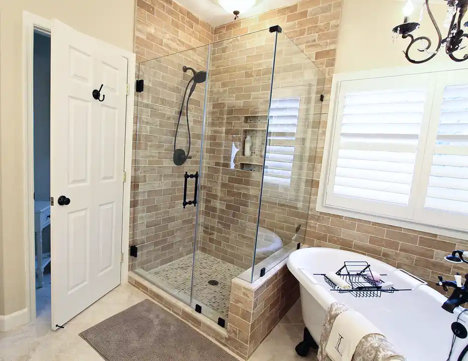 Gainesville VA primary bathroom remodel with glass-enclosed tile shower, clawfoot tub, plantation shutters, and dark bronze fixtures