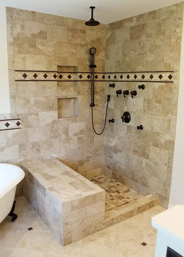 Gainesville VA primary bathroom remodel with walk-in tile shower, recessed niches, bench wall, decorative accent band, and dark bronze fixtures