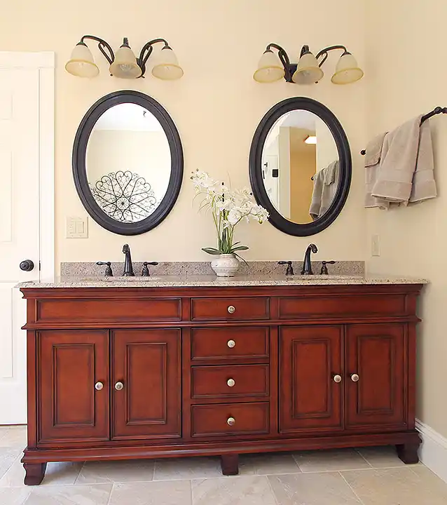 Haymarket VA primary bathroom remodel with cherry double vanity, oval mirrors, granite countertop, and dark bronze fixtures