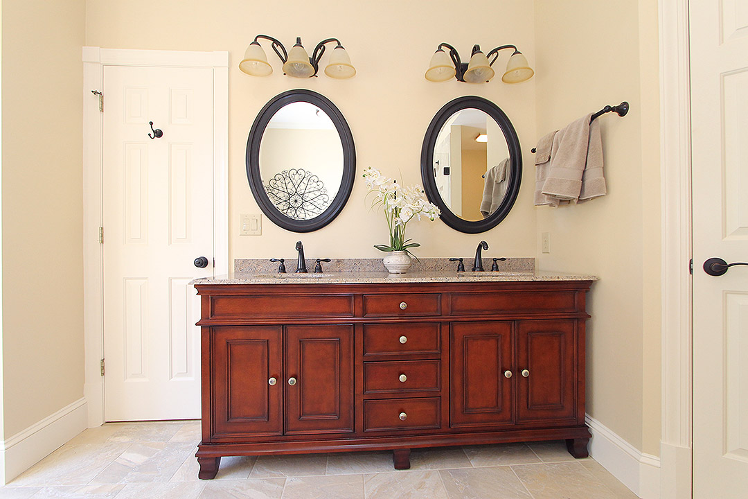 Haymarket VA primary bathroom remodel with cherry double vanity, oval mirrors, granite countertop, and dark bronze fixtures