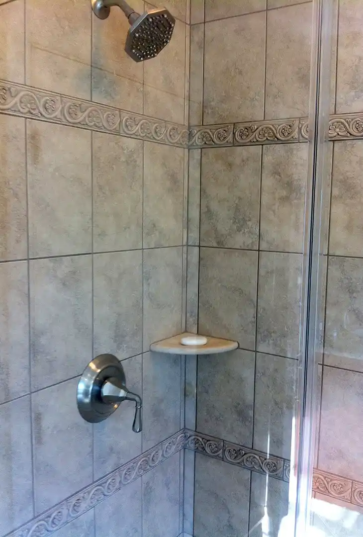 Haymarket VA primary bathroom remodel with tiled shower, decorative accent tile, corner shelf, glass door, and brushed nickel shower fixtures