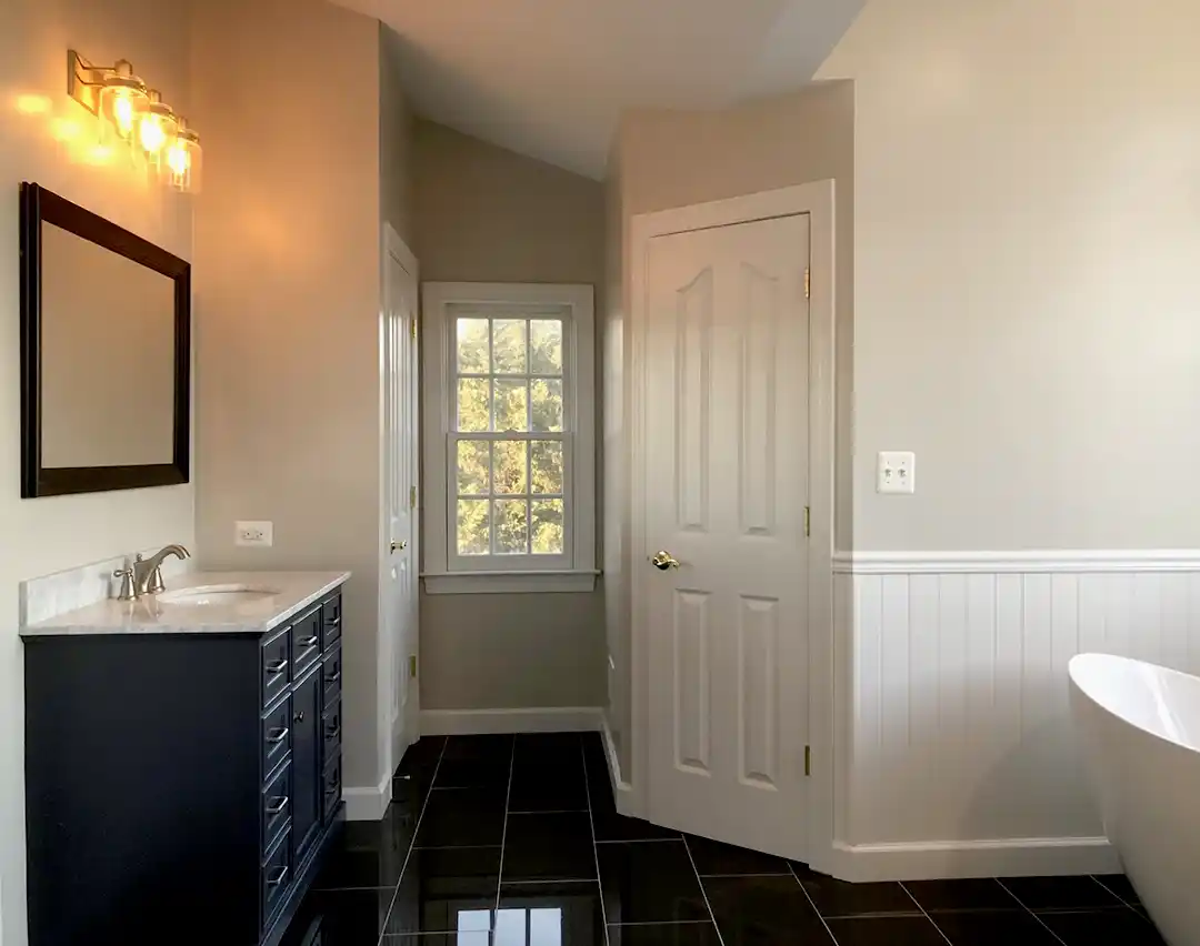 Manassas VA primary bathroom remodel with dark vanity, marble-look countertop, freestanding tub, beadboard wainscoting, and black floor tile