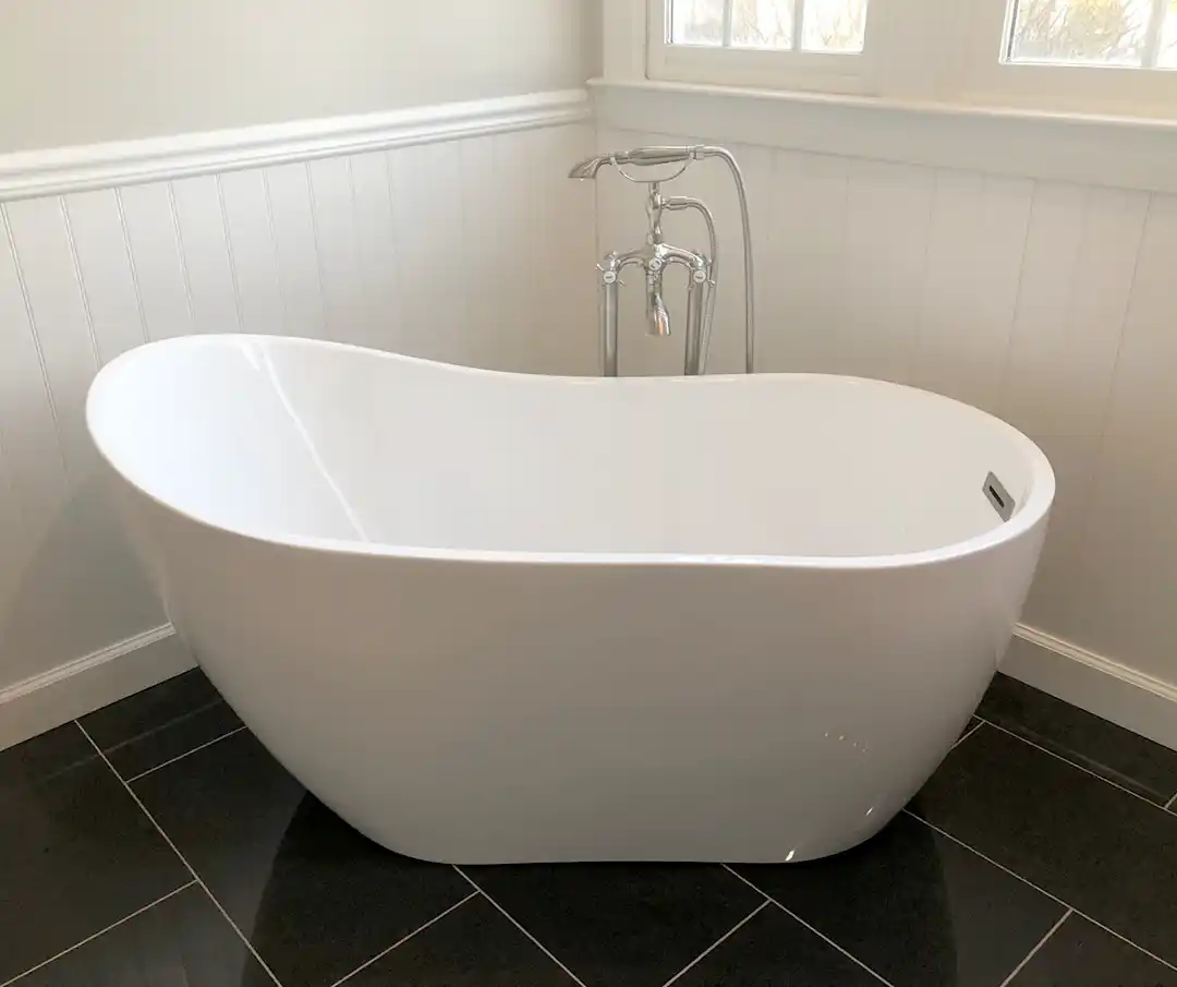 Manassas VA primary bathroom remodel with freestanding white soaking tub, chrome tub filler, beadboard wainscoting, and black floor tile
