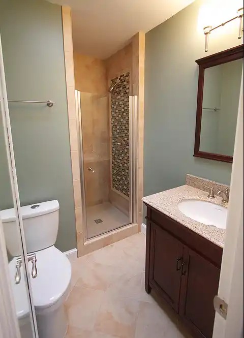 McLean VA bathroom remodel with tile shower, mosaic accent wall, glass shower door, wood vanity, and granite-look countertop