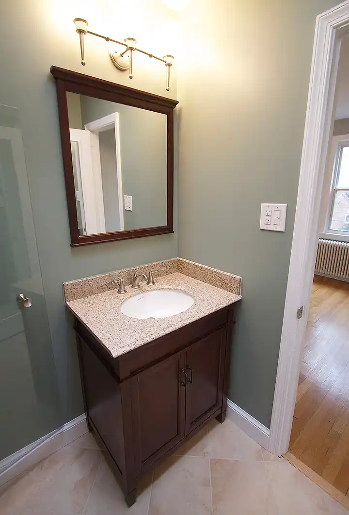 McLean VA bathroom remodel with wood vanity, granite-look countertop, framed mirror, brushed nickel faucet, and warm neutral floor tile
