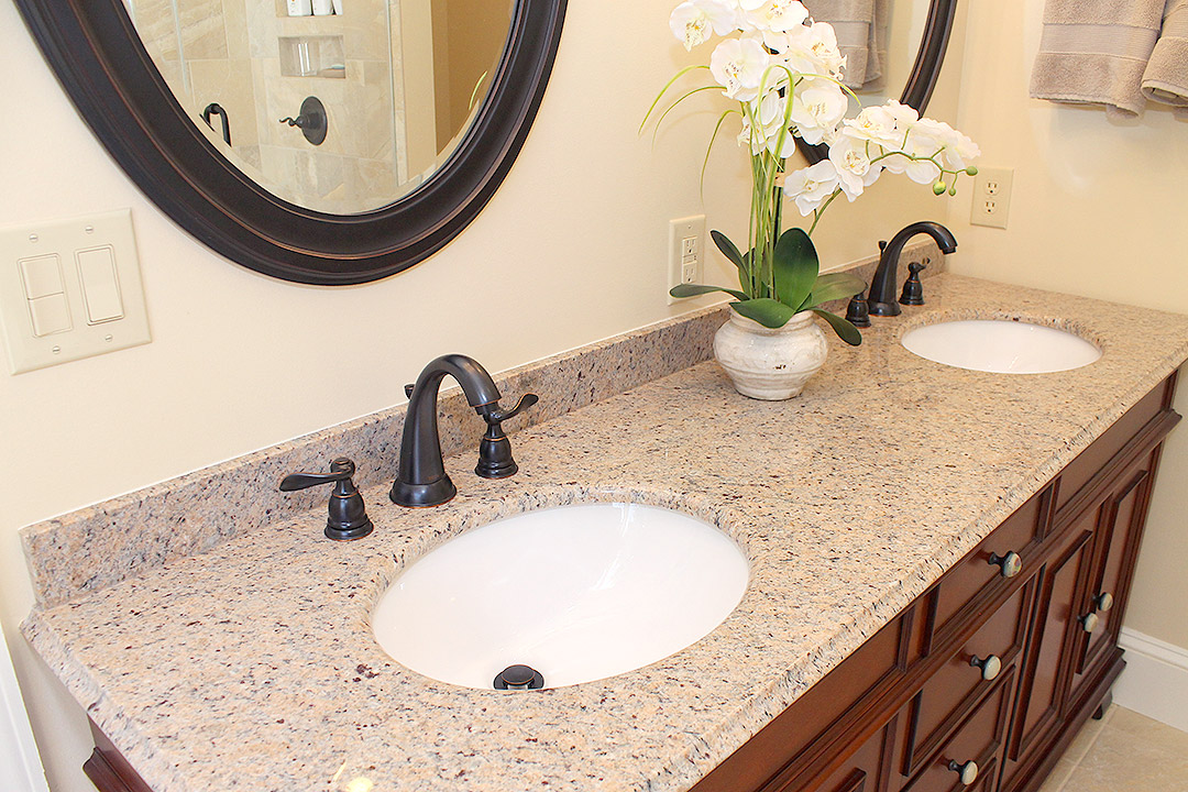 Haymarket VA primary bathroom remodel with cherry double vanity, oval mirrors, granite countertop, and dark bronze fixtures